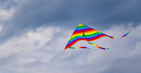 A bright multi-colored kite flies in the air against a cloudy evening summer sky