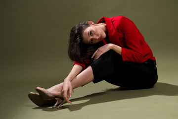 Fototapeta na wymiar A sensual young woman in a red jacket, culottes and shoes with wet long black hair poses against a green background in the studio.