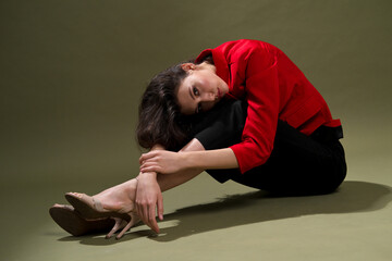 Fototapeta na wymiar A sensual young woman in a red jacket, culottes and shoes with wet long black hair poses against a green background in the studio.