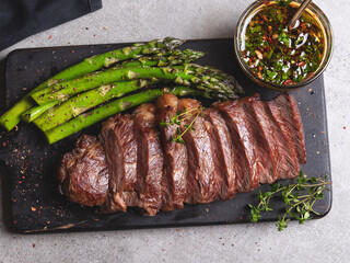 juicy grilled sliced beef steak, with roasted asparagus, close up, sauce, wooden board