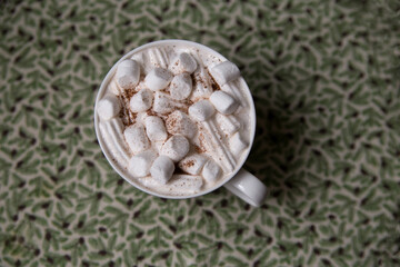 
A white cup with hot chocolate and marshmallows stands on a Christmas tablecloth