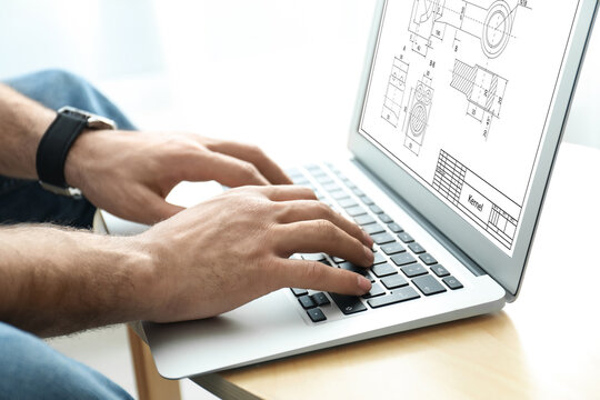 Male engineer working with technical drawing on laptop at table, closeup