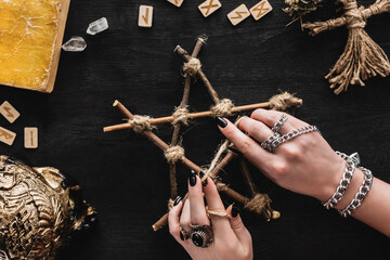 top view of witch touching pentagram near runes, book, crystals, skull and voodoo doll on black