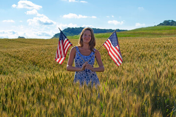 Flower dress young proud smiling happy girl with two red white blue star USA American flags in the hand celebrating Independence Day 4th 4 fourth July on a barley wheat field on sunny day sunset