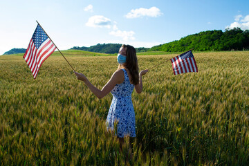 Proud young American girl model wearing n95 face mask with two US USA flags in the hands celebrate Independence Day 4th 4 fourth of July coronavirus pandemic lockdown covid-19 protect health alone