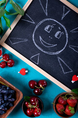 Drawn sun on the chalkboard surrounded by berries against the blue background