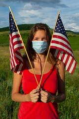 Proud young American girl model wearing n95 face mask with two US USA flags in the hands celebrate Independence Day 4th 4 fourth of July coronavirus pandemic lockdown covid-19 protect health alone