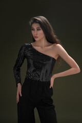 A beautiful young tall girl with long black hair poses in a shiny blouse and black culottes on a green background. Buty and fashion photo shoot.