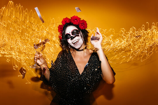 Blissful caucasian girl in zombie attire enjoying wine. Refined female model in halloween outfit drinking champagne with smile.