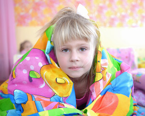 It's a quiet hour. A girl under a blanket looks into the camera. Sleep an hour in kindergarten. 