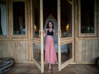 An Asian woman in bamboo tropical house open the bedroom door to see the views. 