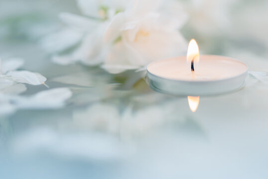 White candle with flowers float on the surface of the water.  Focused on the flame of the candle. SPA. CloseUp. Macro, Defocused. ReflectiCloseUp. Macro, Defocused. Focused on the flame of the candle.