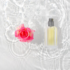 A bottle of perfume in pure waves of water. Flowers and delicate rose petals with drops.