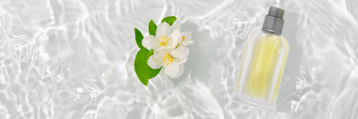 A bottle of perfume in pure waves of water. Flowers and delicate jasmine petals with drops.