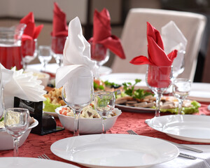 A festive table in a restaurant. Serving table with red tablecloth and white napkins. Serving a restaurant table. Different dishes in white plates on the festive table. Banquet 
