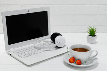 comfortable workplace office - work table with blank white laptop headphones and notebook - home office with a cup of tea or coffee - office desk supplies on light background with brick wall - office 