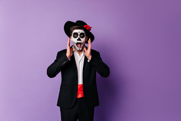Shocked zombie man in elegant clothes posing on purple background in halloween. Surprised guy in...