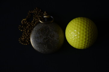 Golf Ball and a classical pocket watch in a black background. Quarantine Photography. Photo captured by Nikon D7000 model Camera and using Nikon AF-S DX NIKKOR 18-140mm f/3.5-5.6G ED VR Lens.
