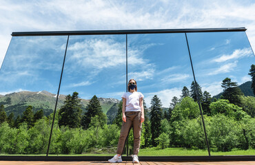Portrait of a girl in a protective mask on a background of nature and mountains. The concept of leisure and vacation in 2020