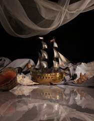Composition with a model of a sailboat and seashells on a glossy table