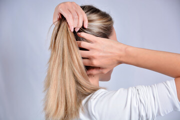 Fototapeta premium Beautiful young woman with blonde shaggy hair change hairstyles with hands. Attractive skinny girl isolated on studio white. Cares about healthy and clean hair. Close up, selective focus