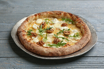 Delicious cheese pizza with walnuts and arugula on grey wooden table, closeup