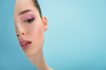 portrait of beautiful woman with glossy lips, pink eyeshadow behind paper round hole isolated on blue