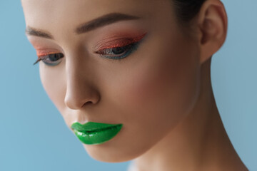 portrait of beautiful woman with green lips, pink and blue eyeshadow isolated on blue