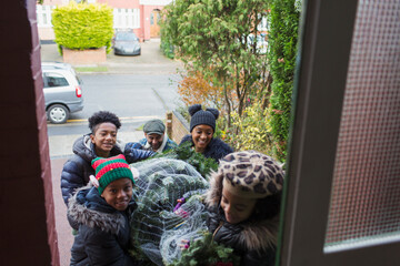 Happy family bringing Christmas tree into front door of house