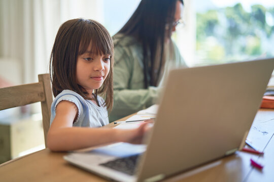 Girl studying on laptop with mother working in background