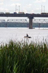 A fisherman on a boat on the Dnieper River in Kiev, Ukraine, close to the Pivnichnyi bridge (ex...