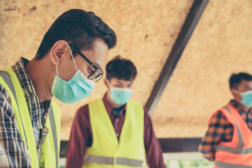 Group of engineering team wear protective face masks safety for Coronavirus Disease 2019 (COVID-19) meeting to plan for new project  measuring layout of building blueprints in construction site.