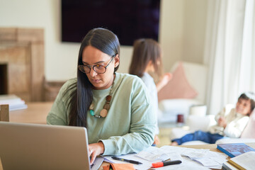 Mother paying bills on laptop with kids playing in background