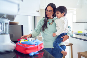 Mother holding son and preparing school lunch in kitchen