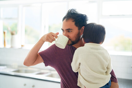 Man drinking coffee and holding son in morning kitchen