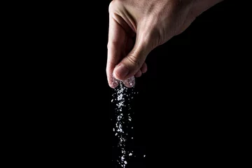 Poster Male hand sprinkles salt on a black background. Cooking concept. © Ruzanna