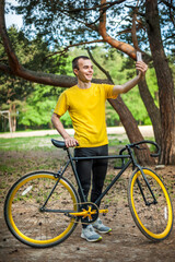 Naklejka premium A young man taking a selfie with his Bicycle. In a public Park, among trees and vegetation.