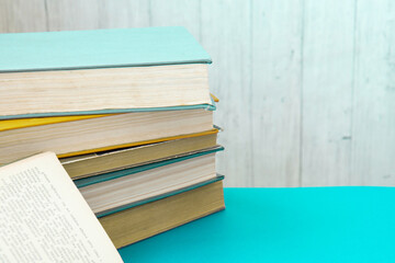 Old and well used hardback books and open book. Back to school. Many Books Piles. Hardback books on turquoise table. Stack of colorful books. Side view. Copy space for text