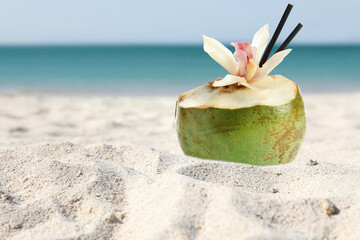 Green coconut with refreshing drink on sandy beach