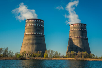 Two cooling towers of a nuclear power plant near a lake against a blue sky. Ecological energy...