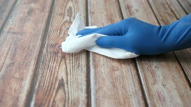 Man hand in blue gloves cleaning wooden surface 