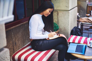 Beautiful asian journalist with long black hair studying while writing some notes in notebook and...