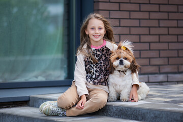 A cute smiling blonde girl of 9 years old gently hugs a dog.