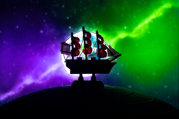 Beautiful boat toy over a blue balll with blurred violet and green planet and cosmos scene at...