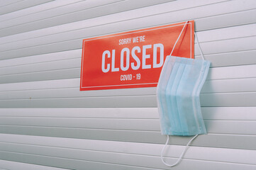 Red plate Sorry We're Closed COVID-19 with medical mask hanging on the door.