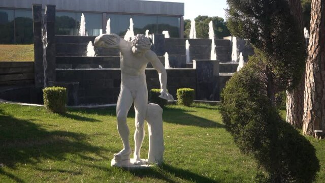 A white statue in the background of decorative fountain. Water flows over large artificial stones. Landscape design.