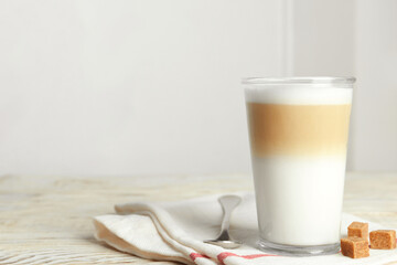 Delicious latte macchiato and sugar cubes on white wooden table indoors, space for text