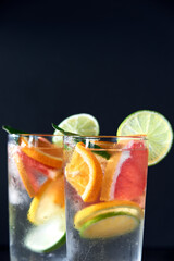 Health care, fitness, healthy nutrition diet concept. Fresh cool homemade citrus infused detox water with grapefruit, orange, lemon and lime and ice in glasses on dark background.