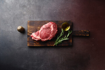 Top view of raw black angus prime rib eye beef steak on wooden cutting board.