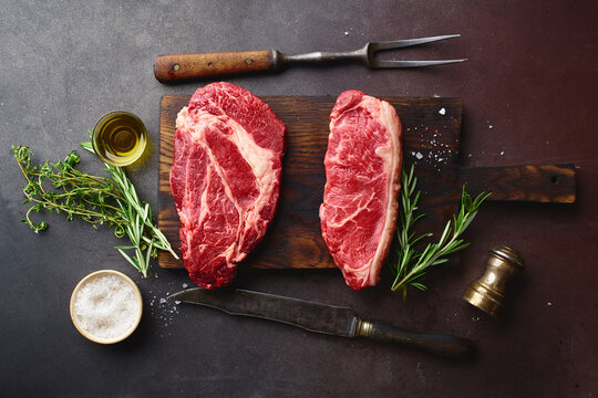 Top view of raw black angus prime beef steaks on wooden cutting board: chuck roll and striploin.